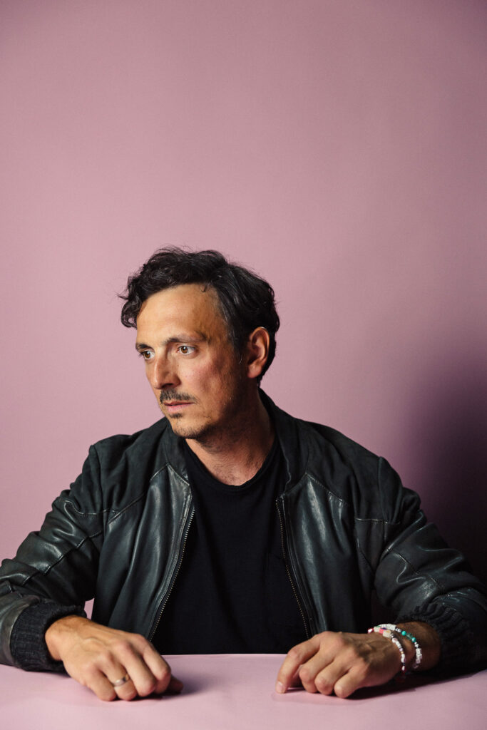 Zdjęcie półprofil profilowe portretowe aktora Piotra Franasowicza, poważna twarz, ręce przed sobą.