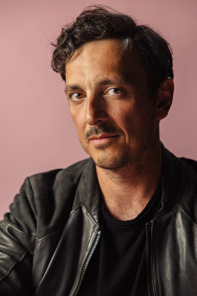 Zdjęcie półprofil profilowe portretowe aktora Piotra Franasowicza, poważna twarz, bliski kadr.