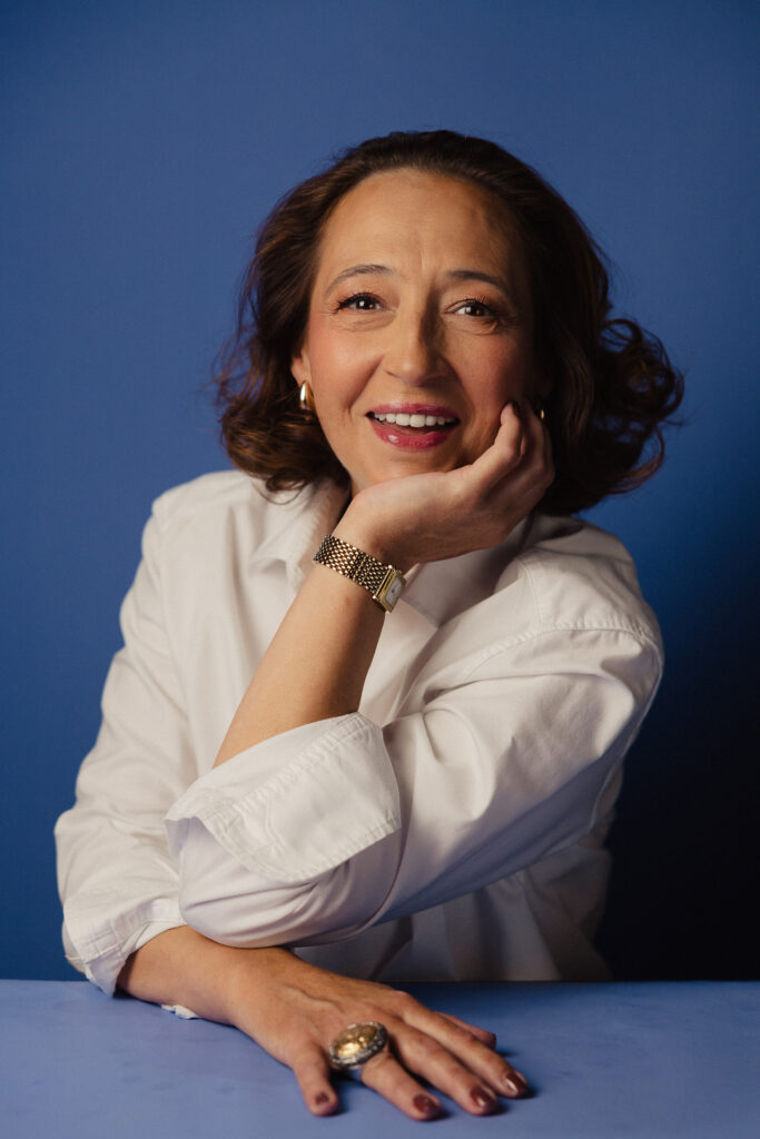 Zdjęcie portretowe aktorki Marty Bizoń, szeroki uśmiech, ręka podpiera twarz.