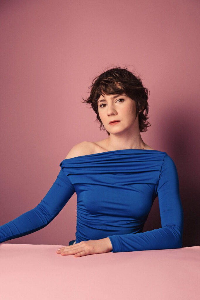 Zdjęcie portretowe aktorki Marii Chojnackiej, poważna twarz, bliski kadr, ręce luźno przy sylwetce.