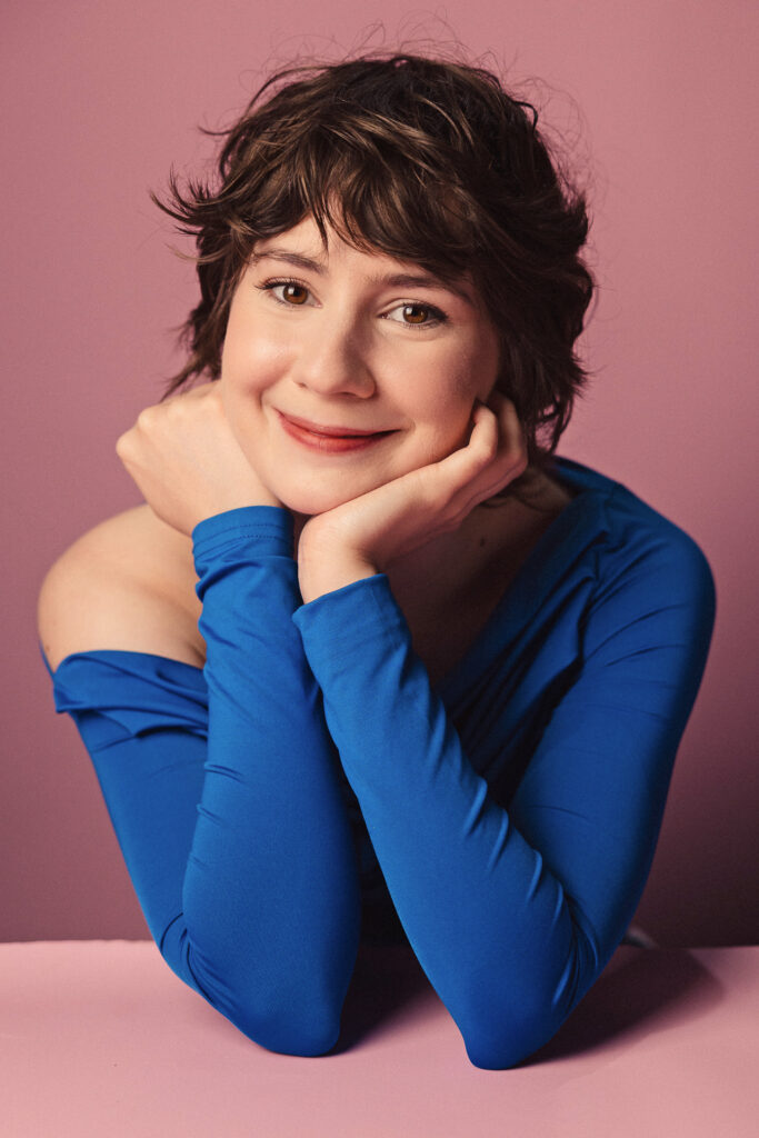 Zdjęcie portretowe aktorki Marii Chojnackiej, lekki uśmiech, ręce podpierają brodę.