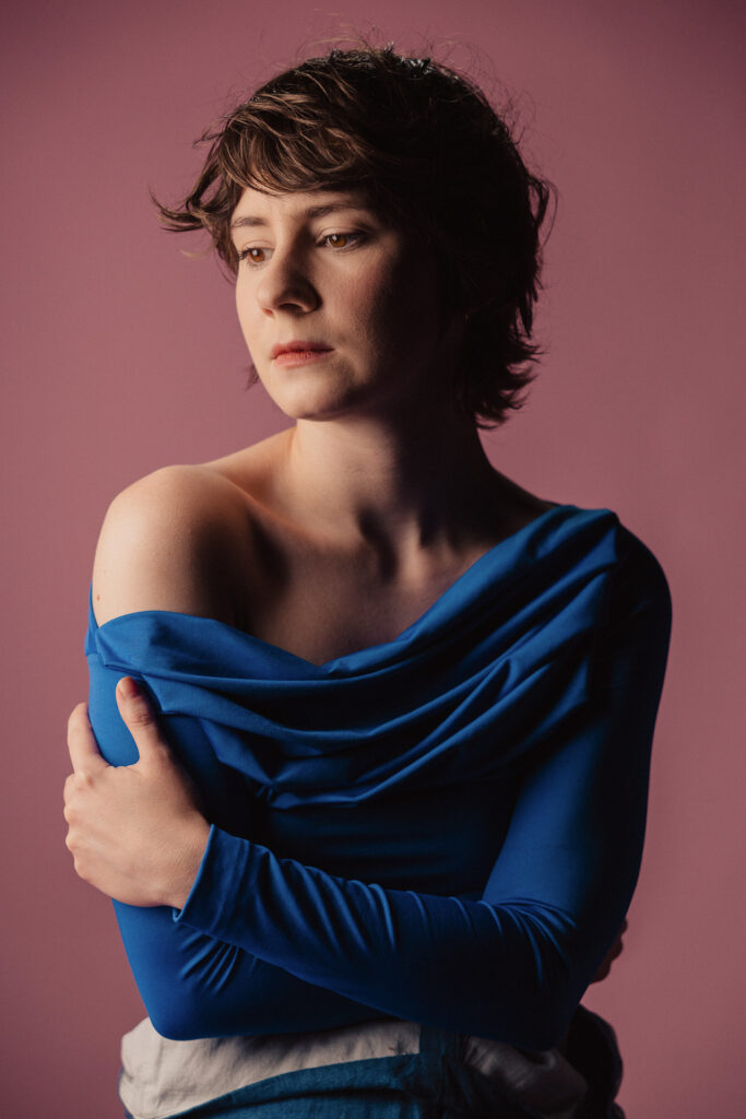 Zdjęcie półprofil portretowe aktorki Marii Chojnackiej, poważna twarz, bliski kadr, ręce otulają sylwetkę.