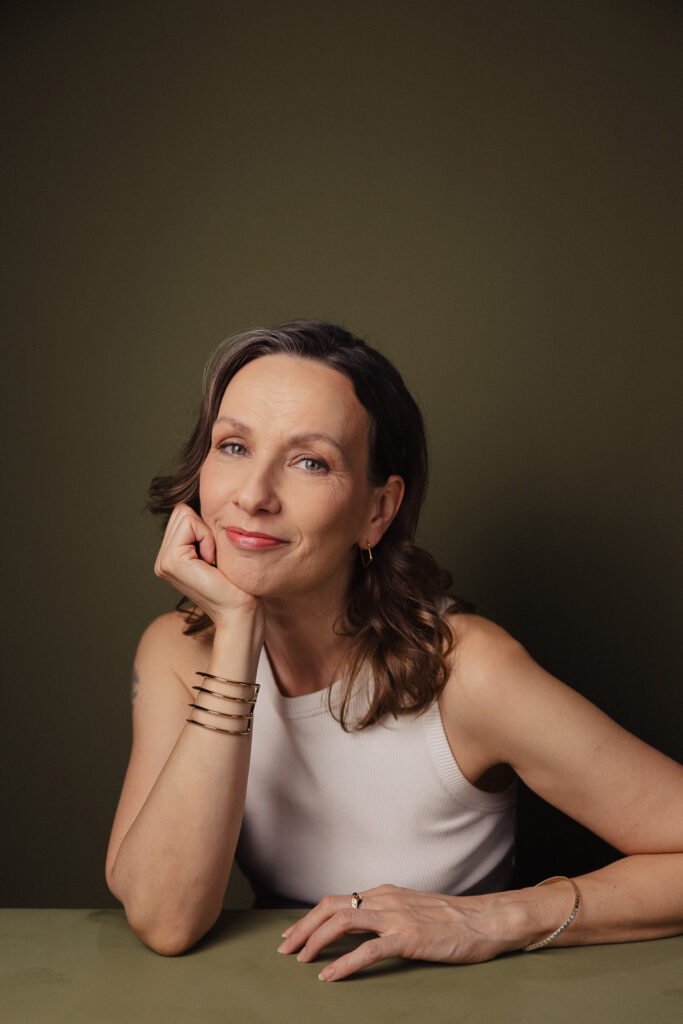 Zdjęcie półprofil portretowe aktorki Patrycji Durskiej, lekki uśmiech, ręka podpiera brodę.