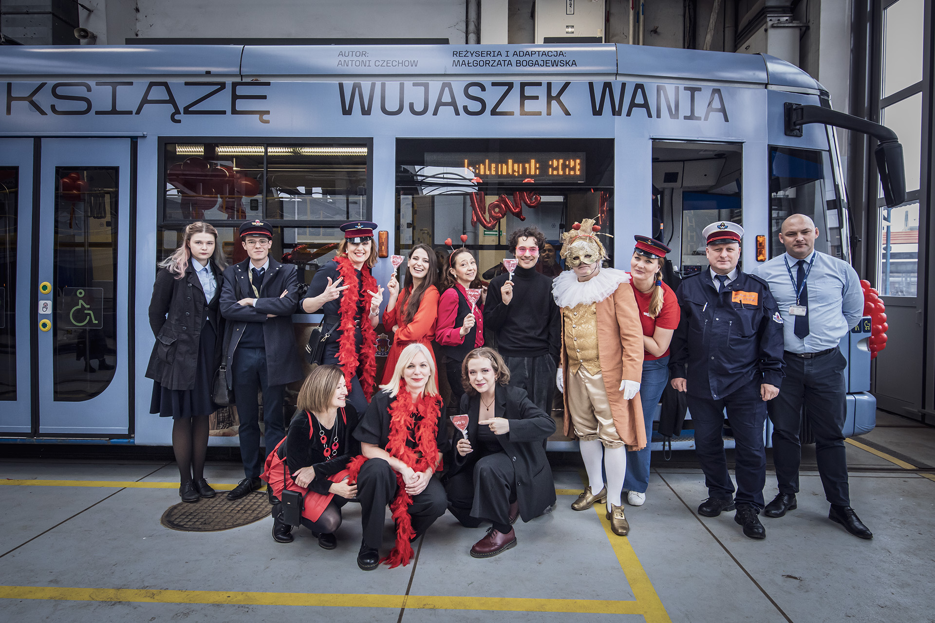 Zdjęcie grupowe przed walentynkowym tramwajem. Część osób z akcentami czerwonymi, uśmiechają się. Część w strojach motorniczych.