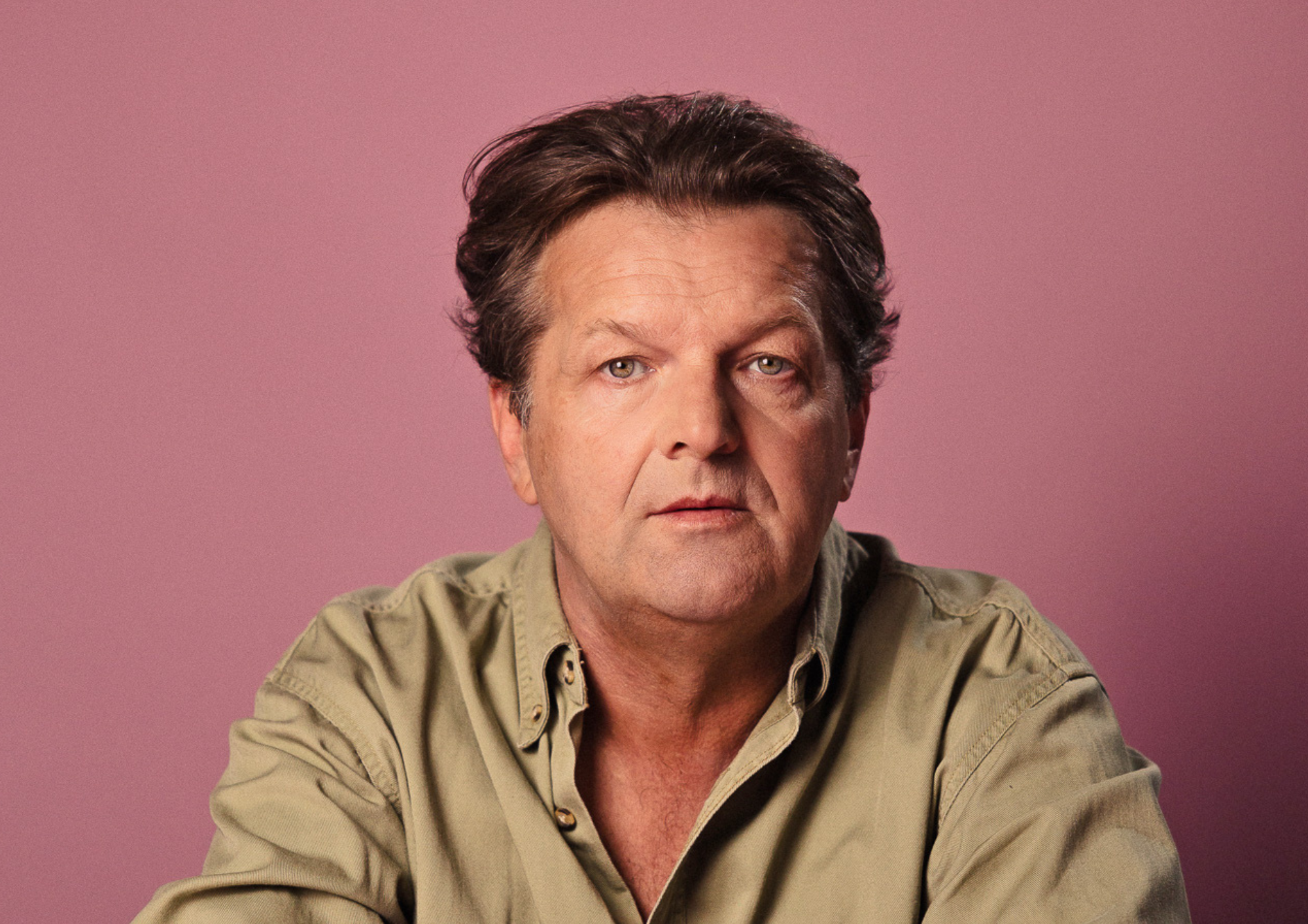 Zdjęcie portretowe aktora Jacka Wojciechowskiego, poważna twarz, ręce skrzyżowane przed sobą.