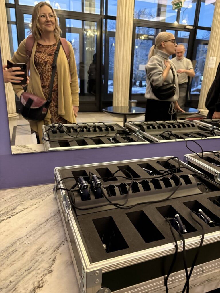 Na blacie leży duże pudło profesionalnie przechowujące słuchawki do audiodeskrypcji, w lustrze w tle odbijają się ludzkie postaci.