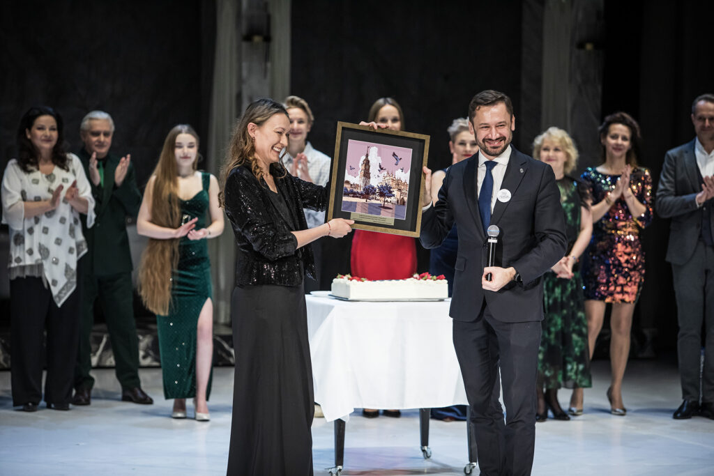 Zdjęcie grupowe, na scenie z rąk Prezydenta Miasta Krakowa , Dyrektor Małgorzata Bogajewska odbiera symboliczny prezent jubileuszowy/ obraz.