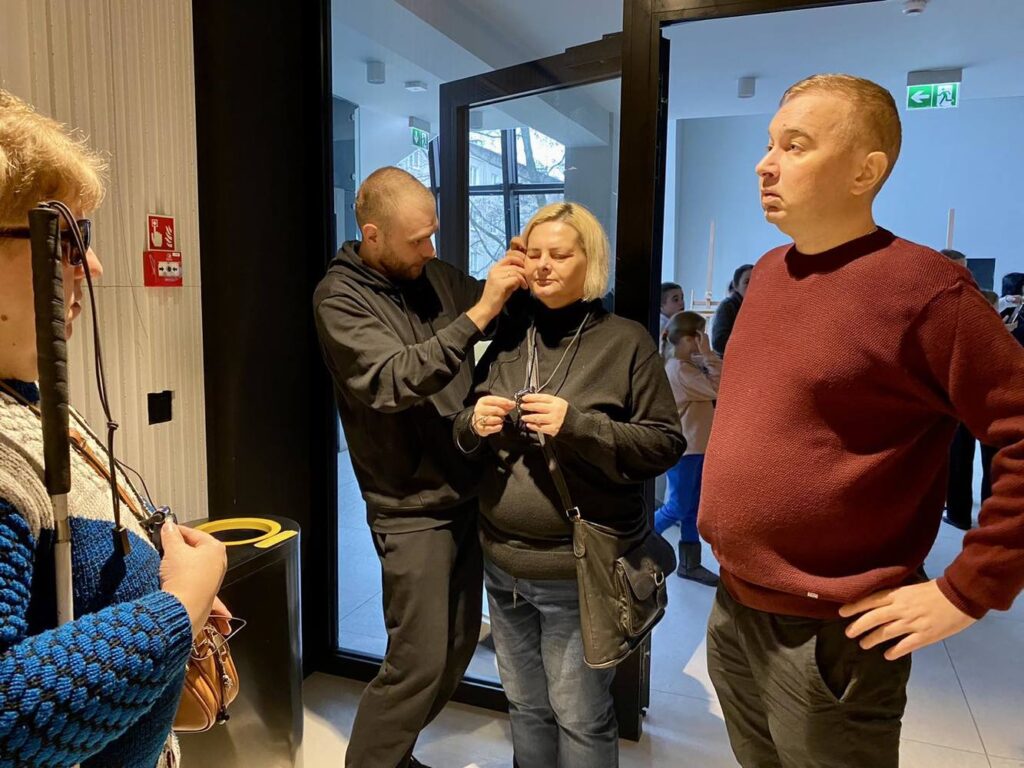 Osoba techniczna zakłada słuchawki do audiodeskrypcji kobiecie.