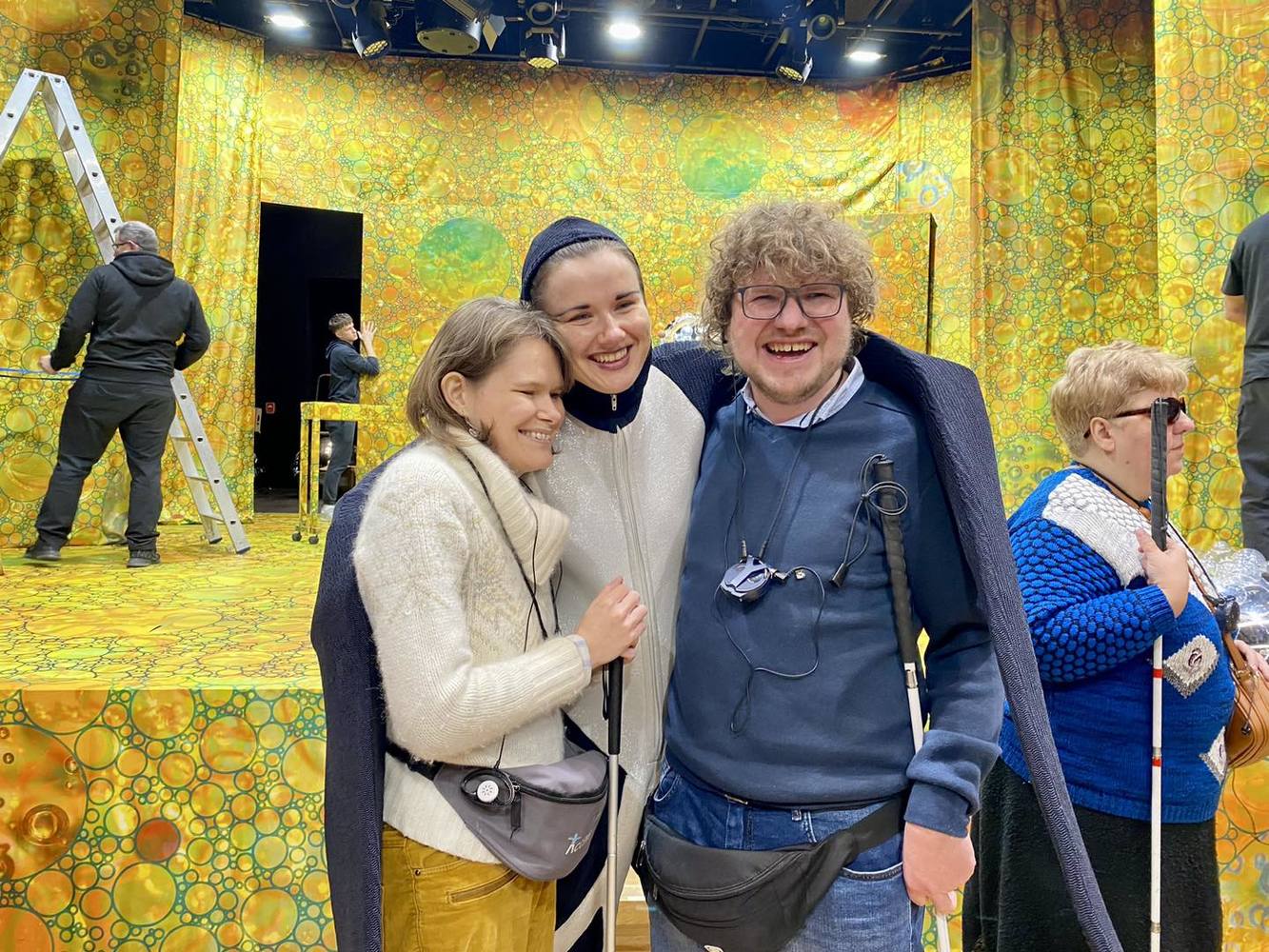 Przed sceną stoi aktorka w stroju jaskółki, skrzydłami obejmuje kobietę i mężczyznę.