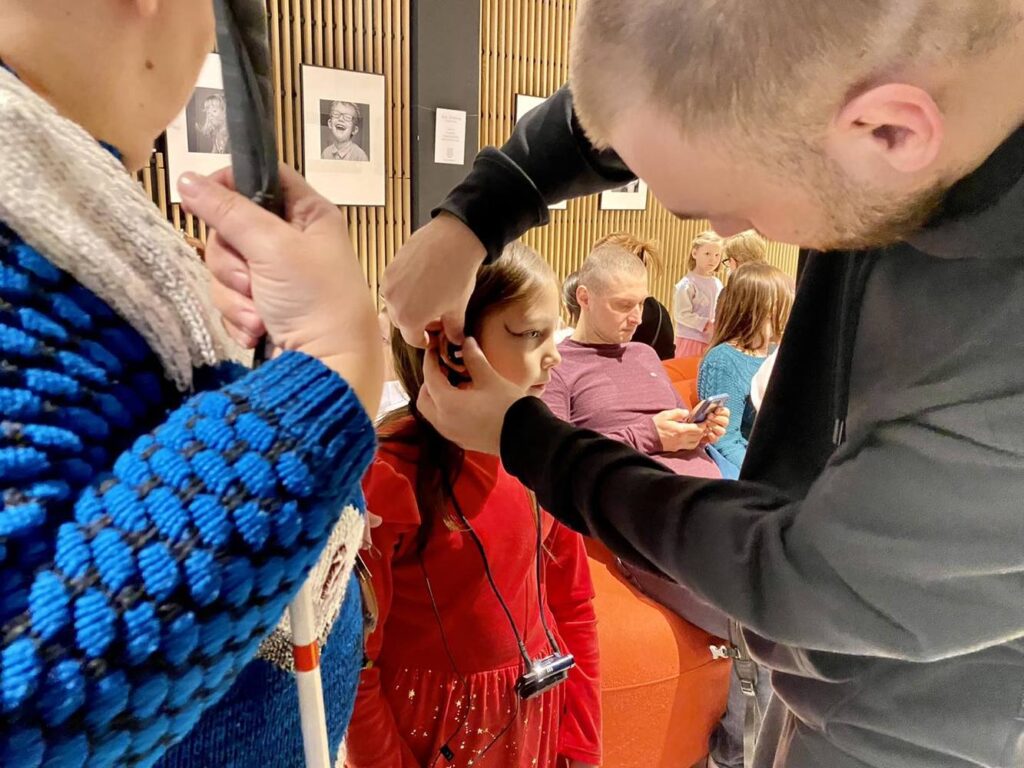 Zbliżenie na zakładanie słuchawek do audiodeskrypcji małej dziewczynce.
