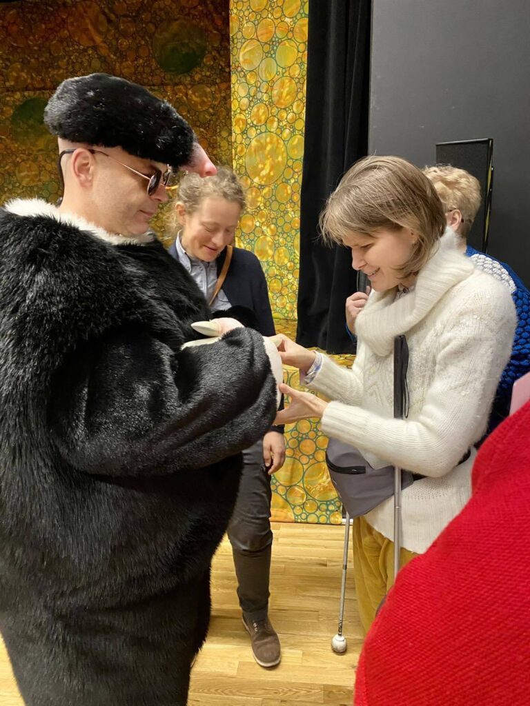 Grupa ludzi, w centralnym punkcie aktor w futrzastym stroju kreta, prezentuje zebranym walory swojego kostiumu.