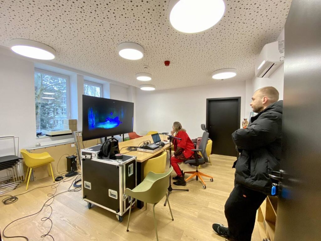 Duży pokuj, przed monitorem i komputerem siedzi lektorka, za jej plecami stoi osoba techniczna.