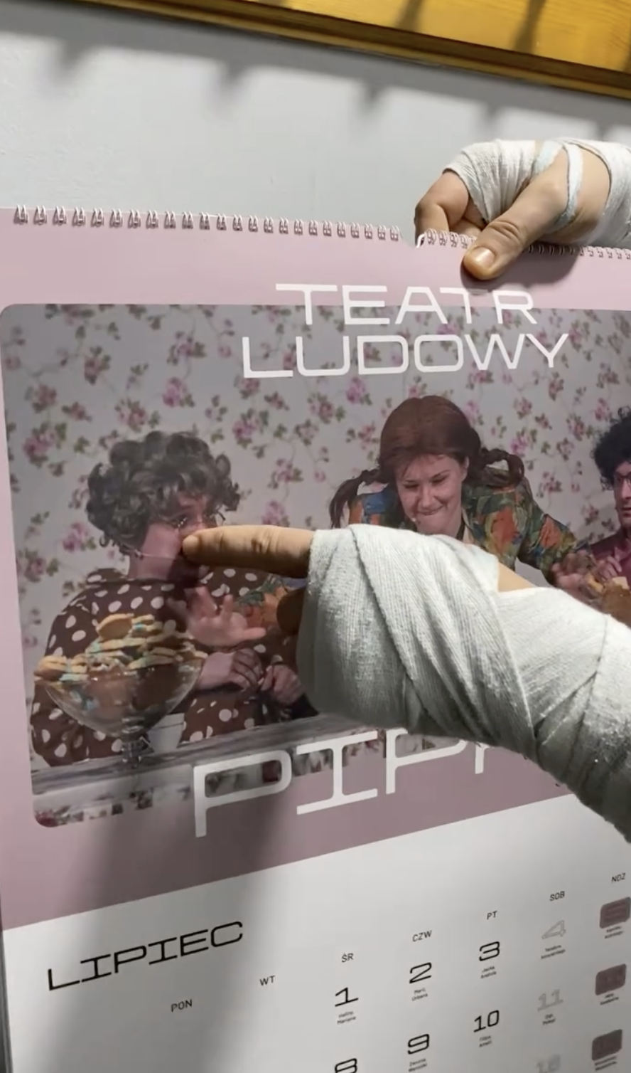 Zbliżenie na rękę wskazującą na zdjęciu w kalendarzu aktora w stroju kobiety - ręka jest obandażowana