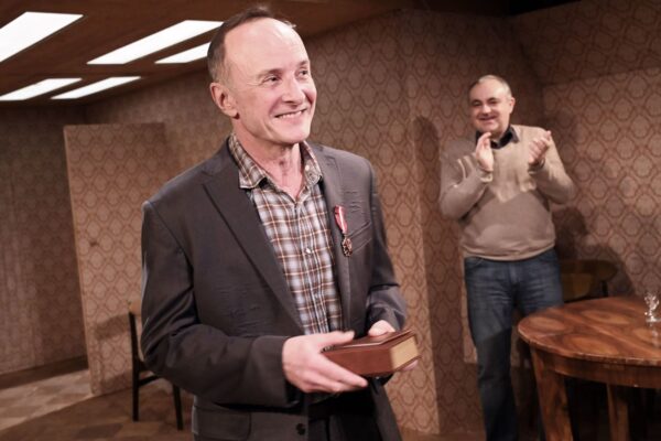 Aktor Piotr Pilitowski stoi na scenie ma do piersi przypięty medal.
