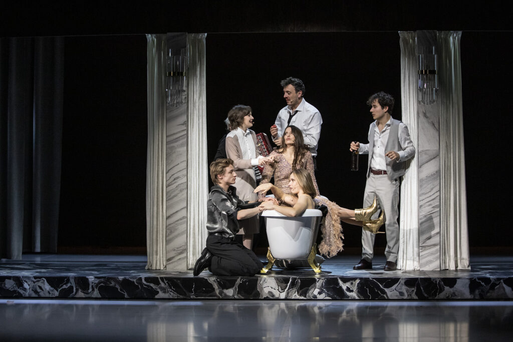 Zdjęcie ze spektaklu Uroczystość. W centrum sceny stoi wanna , grupa młodych aktorów, siedzi w wannie, piją alkohol.