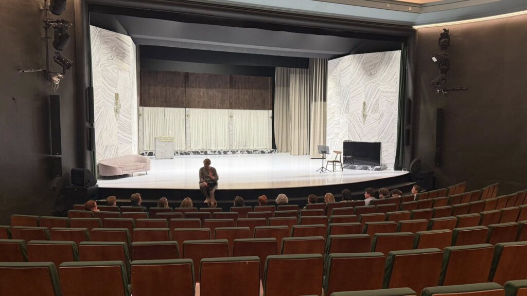 Widok na Scenę i widownię, w pierwszym rzędzie siedzi grupa ludzi, na brzegu sceny siedzi lektorka.