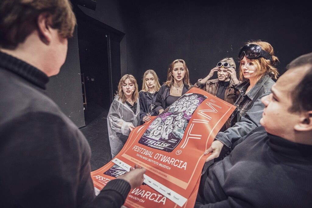 Zdjęcie z pierwszej edycji Festiwalu Otwarcia. Grupa młodzieży trzyma plakaty Festiwalu Otwarcia. Na plakacie są graficzne portrety młodzieży i czerwone tło.