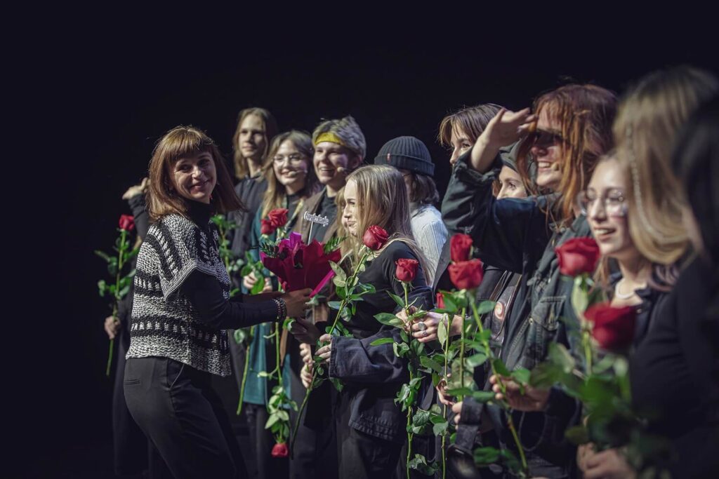 Zdjęcie z pierwszej edycji Festiwalu Otwarcia. Młodzież w kostiumach stoi w rzędzie z różami, uśmiechają się, przed nimi stoi kobieta z kwiatami.