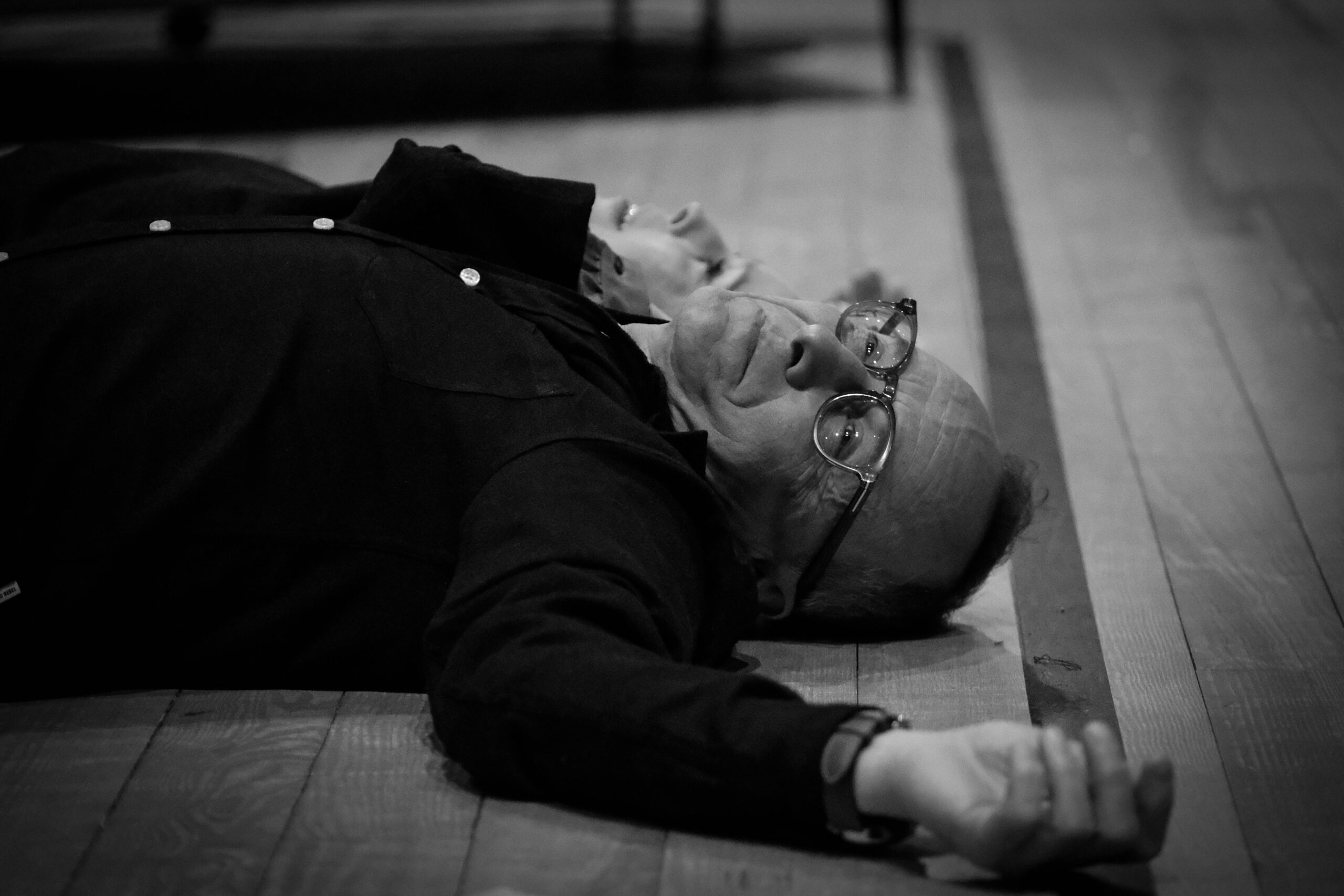 Czarnobiałe zdjęcie, aktor z rozłożonymi rękami leży na podłodze- bliski kadr.